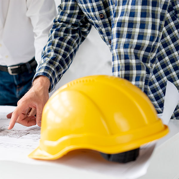JGV Ingeniería - ingeniería civil en Málaga Fotografía de dos personas trabajando sobre unos planos con un casco de obra amarillo