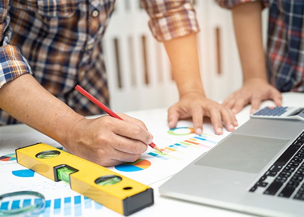 Fotografía de dos personas trabajando sobre papel con infografías, con un nivel y un portátil en la mesa